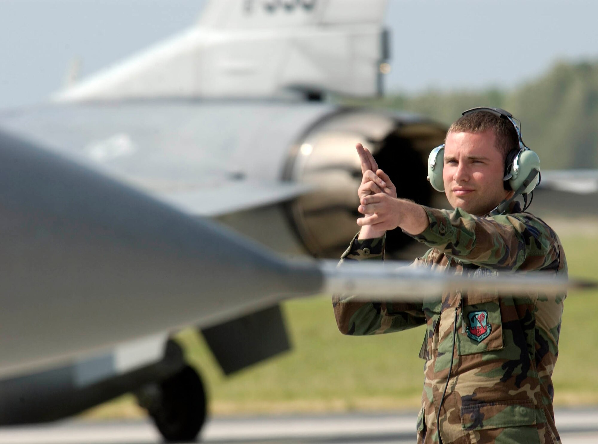 POZNAN, Poland -- Senior Airman Sean Kaley guides an F-16 Fighting Falcon while another taxis in the background.  Airmen from the Illinois Air National Guard's 183rd Fighter Wing are familiarizing Polish airmen with the F-16 during the U.S. European Command exercise Sentry White Falcon 2005 through June 17.  In 2006, the Polish air force will start receiving their own F-16s that will begin replacing their Soviet-made MiG fighters as the country modernizes its military to NATO standards.  Airman Kaley is a crew chief with the wing.  (U.S. Air Force photo by Master Sgt. John E. Lasky)