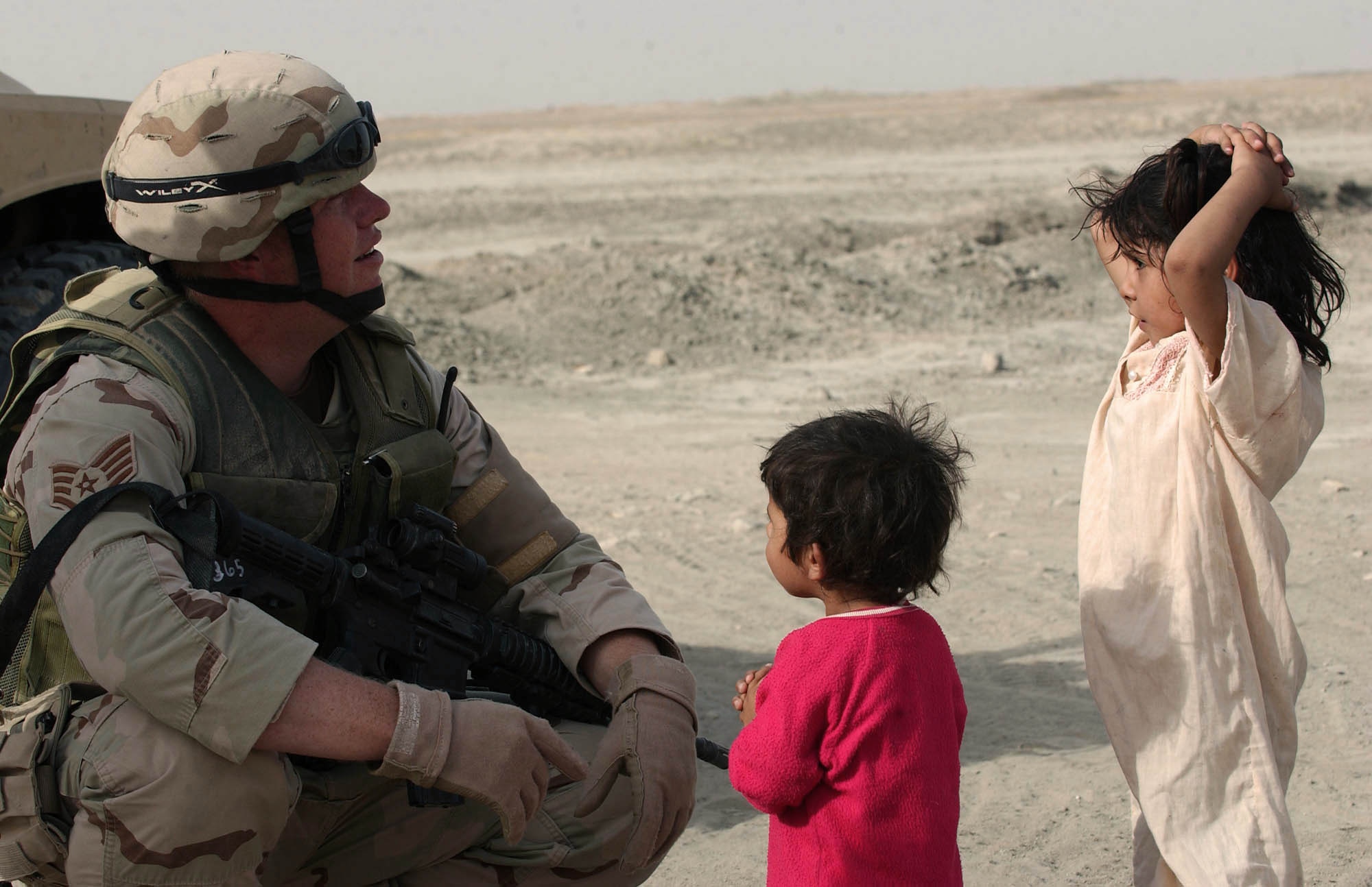 IRAQ -- Staff Sgt. James Partin talks to local children during an Operation Kaleidoscope mission recently.  The new program adds extra protection to perimeter defense procedures and gives locals a point of contact to call if they see suspicious activity that could harm U.S. or coalitions forces.  Sergeant Partin is assigned to the 407th Expeditionary Security Forces Squadron at nearby Tallil Air Base.  (U.S. Air Force photo by Master Sgt. Maurice Hessel)