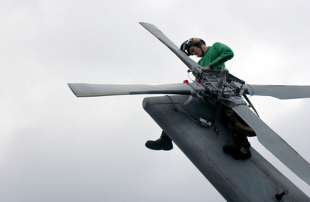 Petty Officer 3rd Class Adam Barber perches on the tail of an SH-60F Seahawk as he replaces the helicopter's anti- collision light aboard the aircraft carrier USS Nimitz (CVN 68) on June 10, 2005. Barber is a Navy Aviation Electrician's Mate assigned to Helicopter Anti-Submarine Squadron 6 deployed onboard the Nimitz from Naval Air Station North Island, San Diego, Calif. 