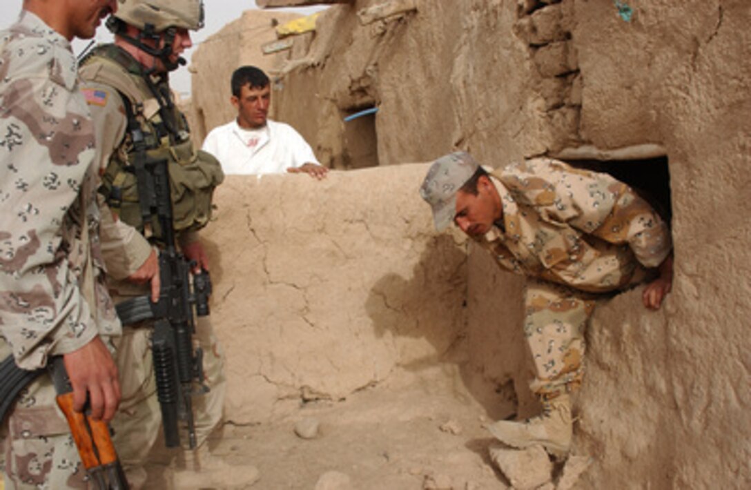 Montana Army National Guardsman Sgt. Terry Morgan (2nd from left) watches as an Iraqi Army soldier emerges from an earthen hut in the Riyadh District of Iraq on May 24, 2005. Morgan, his fellow Guardsmen from Charlie Company, 116th Engineer Battalion, Task Force 1-163rd Infantry and Iraqi Army soldiers are searching villages for weapons caches and signs of insurgents. 