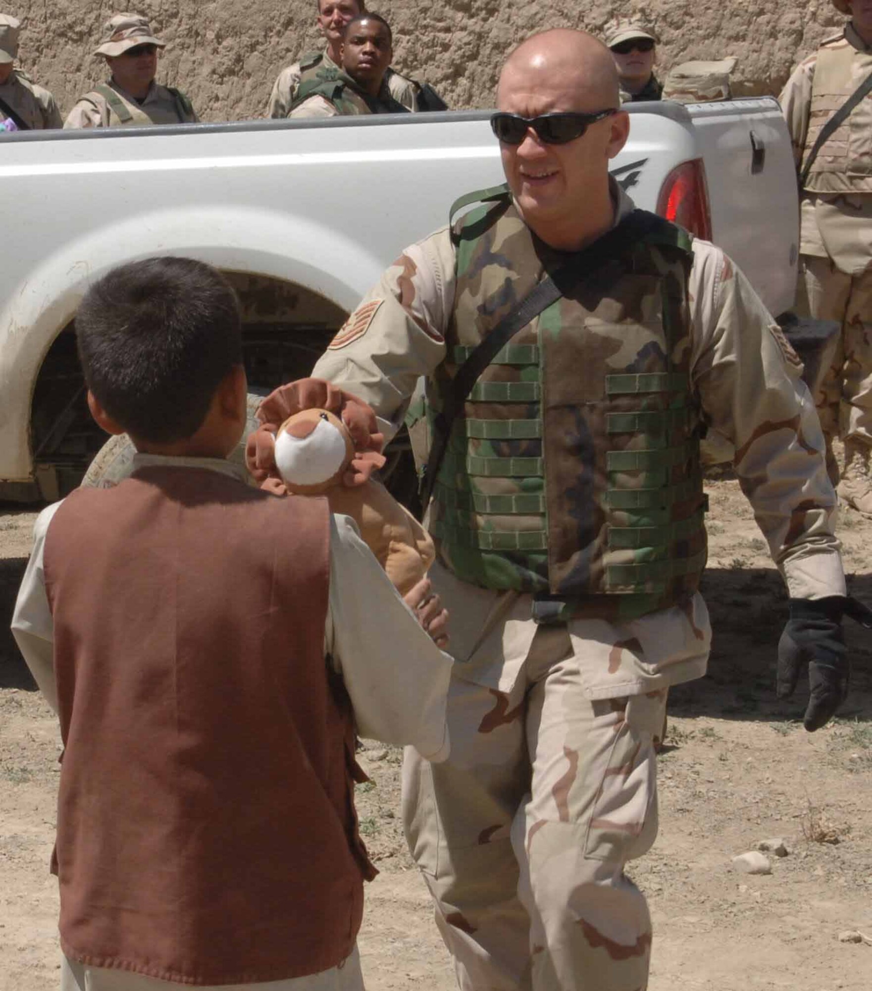 PARWAN PROVINCE, Afghanistan -- Tech. Sgt. Antonio Guitron hands an Afghan boy a stuffed animal during an adopt-a-village trip here.  Airmen from the 455th Air Expeditionary Wing at nearby Bagram Air Base take part in the program to assist villages in Afghanistan with infrastructure, fresh water, school supplies and toys for children.  Sergeant Guitron is the noncommissioned officer in charge of the 455th Expeditionary Services Squadron and is deployed from Luke Air Force Base, Ariz.  (U.S. Air Force photo by Capt. Mark D. Gibson)
