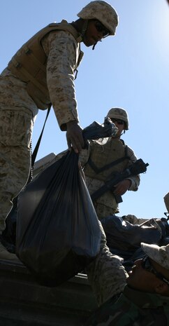 CAMP TAQADDUM, Iraq (March 7, 2005) - Corporal Chaun D. Fitzpatrick, ammunition technician, 1st Force Service Support Group (Forward), passes bags of humanitarian aid supplies to Gunnery Sgt. Robert Sands, anti-terrorism force protection chief, during a civil affairs mission to Al Kabani March 5. Fitzpatrick, a Columbia, S.C., native, said the civil affairs mission was the most exciting thing he did during his seven-month deployment to Iraq. During the mission, Sands, a Baltimore native, and other Marines from the 1st and 2d FSSGs, along with soldiers from the Army's 2nd Battalion, 112th Armor, 36th Infantry, distributed supplies and soccer balls to the town of about 60 homes. (Photo by Cpl. John E. Lawson Jr.)