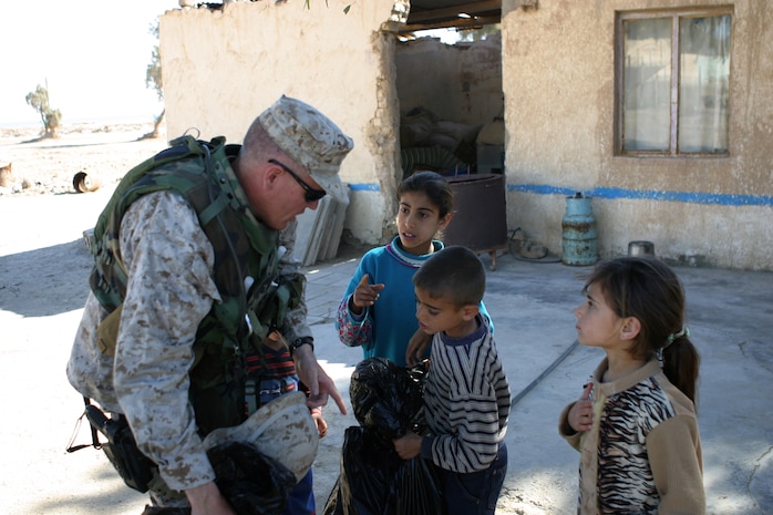 CAMP TAQADDUM, Iraq (March 7, 2005) - Lieutenant Col. Michael H. Gellick, civil affairs officer, 1st Force Service Support Group (Forward), passes bags of humanitarian aid supplies to Iraqi children during a civil affairs mission to Al Kabani March 5. During the mission the Cleveland native and other Marines from the 1st and 2d FSSGs, along with soldiers from the Army's 2nd Battalion, 112th Armor, 36th Infantry, distributed supplies and soccer balls to the town of about 60 homes. (Photo by Cpl. John E. Lawson Jr.)