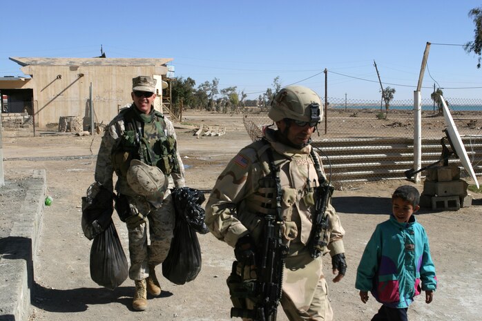 CAMP TAQADDUM, Iraq (March 7, 2005) - Lieutenant Col. Michael H. Gellick, civil affairs officer, 1st Force Service Support Group (Forward) and a Cleveland native, carries bags of humanitarian aid supplies while Army Sgt. Robert Rodriguez, 2nd Battalion, 112th Armor, 36th Infantry, a native of Lorado, Texas, walks with an Iraqi child during a civil affairs mission to Al Kabani March 5. During the mission Marines from the 1st and 2d FSSGs, along with soldiers from the Army's 2/112th, distributed supplies and soccer balls to the town of about 60 homes. (Photo by Cpl. John E. Lawson Jr.)