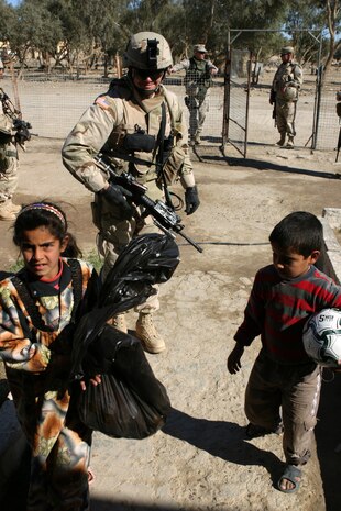CAMP TAQADDUM, Iraq (March 7, 2005) -Army Cpl. Steve H. Branson, a cavalry scout with 2nd Battalion, 112th Armor, 36th Infantry, a native of San Antonio, hands a soccer ball and a bag of humanitarian aid supplies to Iraqi children during a civil affairs mission to Al Kabani March 5. During the mission Marines from the 1st and 2d FSSGs, along with soldiers from the Army's 2/112th, distributed supplies and soccer balls to the town of about 60 homes. (Photo by Cpl. John E. Lawson Jr.)