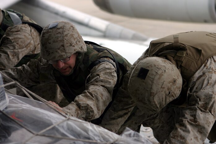 CAMP TAQADDUM, Iraq (March 11, 2005) - Gunnery Sgt. Bryan E. Greenlee, the 2d Force Service Support Group (Forward) postal operations chief, pushes along side his Marines to load outgoing mail onto a plane here March 9.  The Jacksonville, N.C. native is one of 24 Marines who assumed postal responsibilities from 1st FSSG during a mass turn over of troops here in support of Operation Iraqi Freedom. (Photo by Sgt. Kristin S. Jochums)