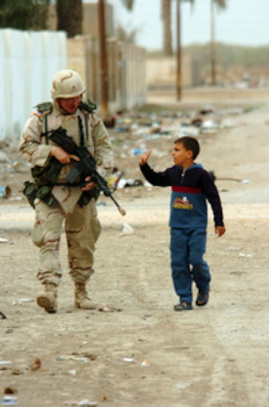 An Iraqi child walks alongside a National Guardsman as he patrols through the neighborhoods of Iskandriyah, Iraq, on March 8, 2005. The Guardsman is from the 155th Brigade Combat Team, Charlie Company, Missouri National Guard, from Tupelo, Miss. 