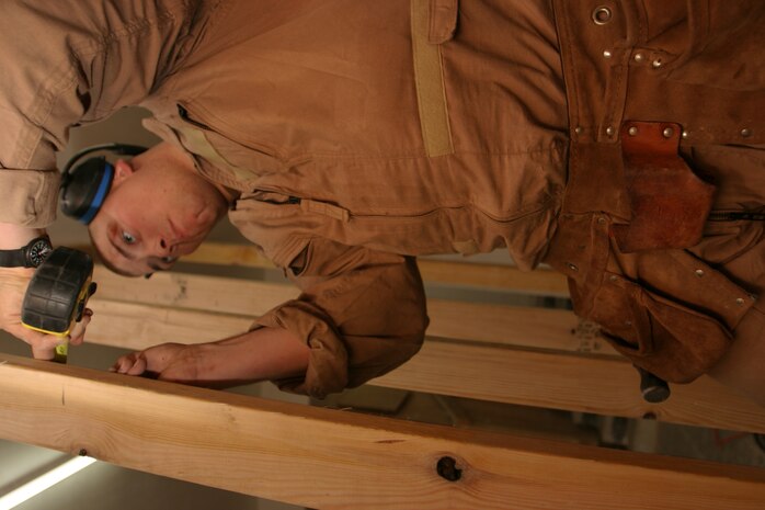 CAMP TAQADDUM, Iraq --Lance Cpl. Brad Feola, a combat engineer with 8th Engineer Support Battalion, 2d Force Service Support Group (Forward), marks the correct measurement on a stud.  Feola, a Boston native, is part of a seven-man team of combat engineers who construct Southwest Asia huts and office spaces for the service members of the base.