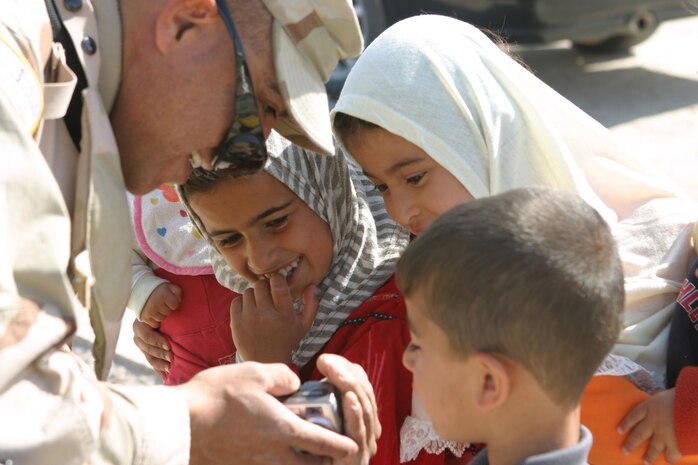 CAMP TAQADDUM, Iraq (March 29, 2005) - Sergeant 1st Class Jesse Ortiz, a San Antonio native and the 2nd Battalion, 112th Armor, 36th Infantry Division civil affairs noncommissioned officer in charge, shows an eager group of Iraqi children their pictures on his digital camera. The 2d Force Service Support Group (Forward) Marines, along with Soldiers visit the local villages of Al Kabani and Quiadisisya to hand out soccer balls and backpacks filled with school supplies. Along with the humanitarian visits, contracts for water towers, septic filtration systems and mosque improvements were agreed upon between the village sheiks and the 2/112th. (Photo by Sgt. Kristin S. Jochums)