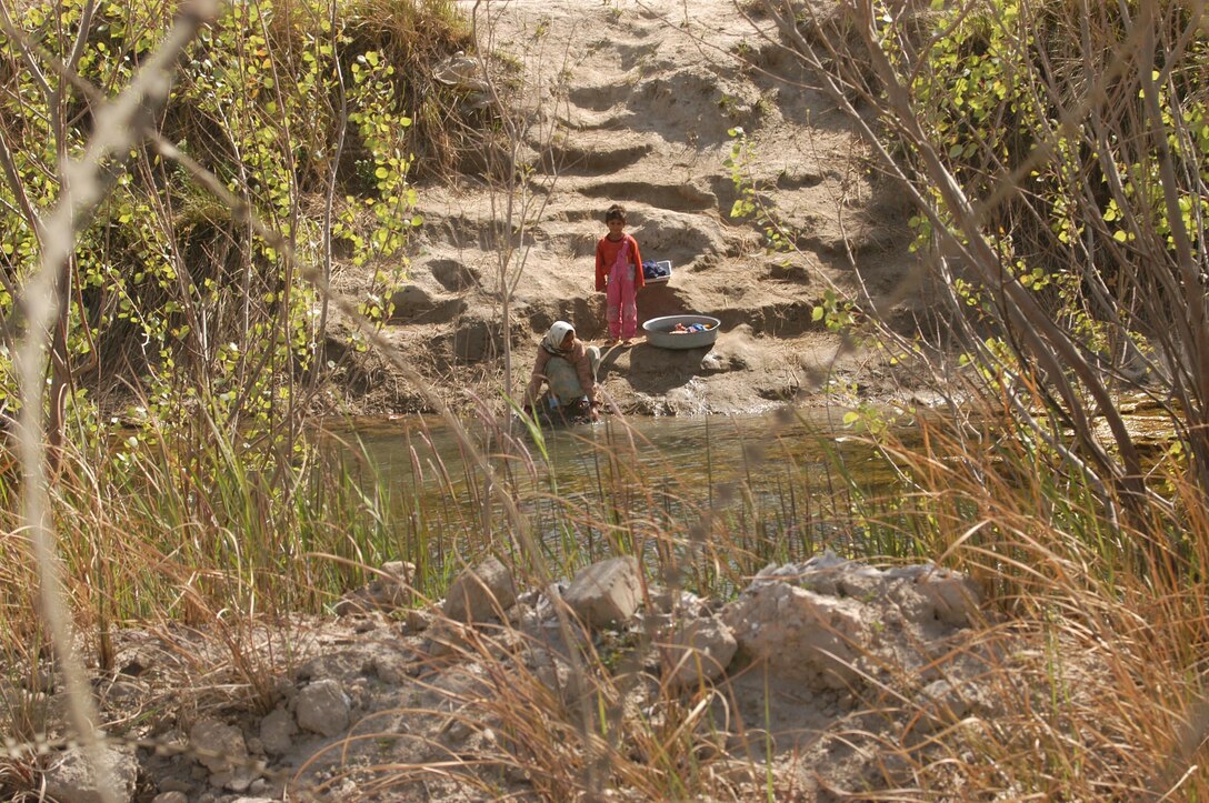 BAGHDAD, Iraq -- (March 24, 2005) - Outside rolls of concertina wire at a vehicle checkpoint manned by 15th Marine Expeditionary Unit (Special Operations Capable) Mairnes and sailors, children wash clothes in a small river as one of their daily chores. The 15th Marine Expeditionary Unit (Special Operations Capable) is currently conducting security and stability operations here in the greater Baghdad area. (Official USMC Photo by Gunnery Sgt. Robert Knoll)