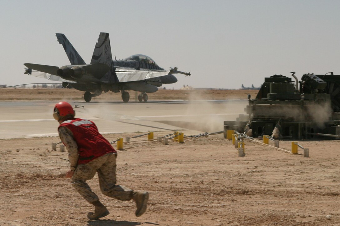 The Marine Corps' only Bengal stripped F/A-18D Hornet, from Marine Fighter Attack Squadron 224, screeches to a halt after hooking on to expeditionary arresting gear. Sgt. James S. Happley, MWSS-271 expeditionary airfield technician, runs to check that both sides of the gear are pulling at the same rate seconds after the Hornet touches down.
