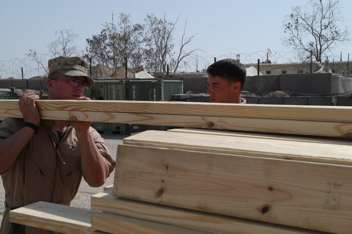 CAMP TAQADDUM, Iraq -- Private First Class Kyle Lefever, a Buffalo, N.Y., native and combat engineer with 8th Engineer Support Battalion, 2d Force Service Support Group (Forward), carries two-by-sixes from where they were dropped off to stack them closer to the job site. Lefever is the newest member of the seven-man team of combat engineers who are building Southwest Asia huts and constructing offices for service members.