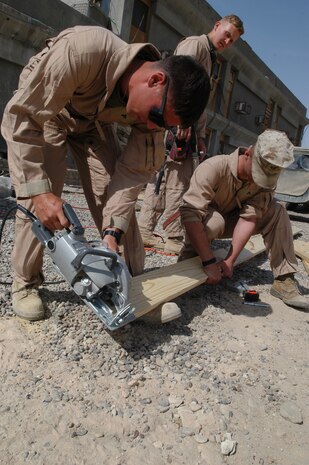 CAMP TAQADDUM, Iraq -- Lance Cpl. Jason Cook, a combat engineer with 8th Engineer Support Battalion, 2d Force Service Support Group (Forward), cuts a two-by-six to the correct length as Pfc. Kyle Lefever helps hold the board.  The St. Louis native, Cook, is part of a seven-man team of combat engineers who construct Southwest Asia huts and office spaces for the service members of the base.
