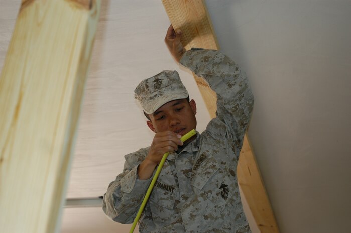 CAMP TAQADDUM, Iraq -- Lance Cpl. Anouphong Chanthamany, a combat engineer with 8th Engineer Support Battalion, 2d Force Service Support Group (Forward), ensures the correct measurement is made for cutting a stud to pressure fit a wall in place between the floor and ceiling.  Chanthamany, a Milwaukee native, is part of a seven-man team of combat engineers who construct Southwest Asia huts and office spaces for the service members of the base.