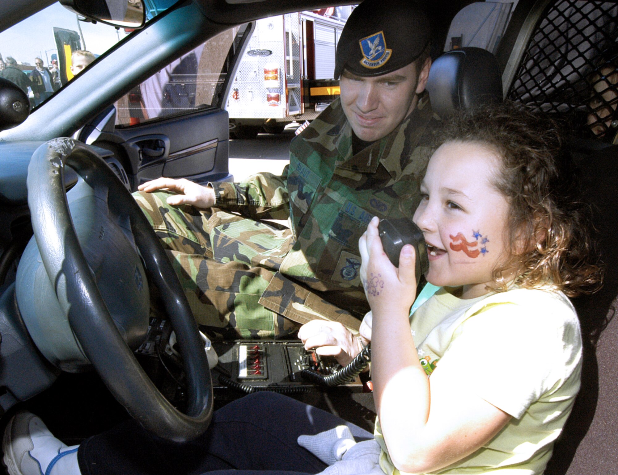TINKER AIR FORCE BASE, Okla. --  Teagan Hamilton, 6,  demands for her dad, aircraft painter Steve Hamilton to "Halt! Put your hands in the air!", during a Bring a Child to Tinker event.  Senior Airman Donald Shaut, assigned to the 72nd Security Forces Squadron, gives children tips on police lingo at the 72nd Security Forces Squadron patrol car display.  The event gave employees a chance to show the children their work world through displays, videos and demonstrations.  (U.S. Air Force photo by Margo Wright)