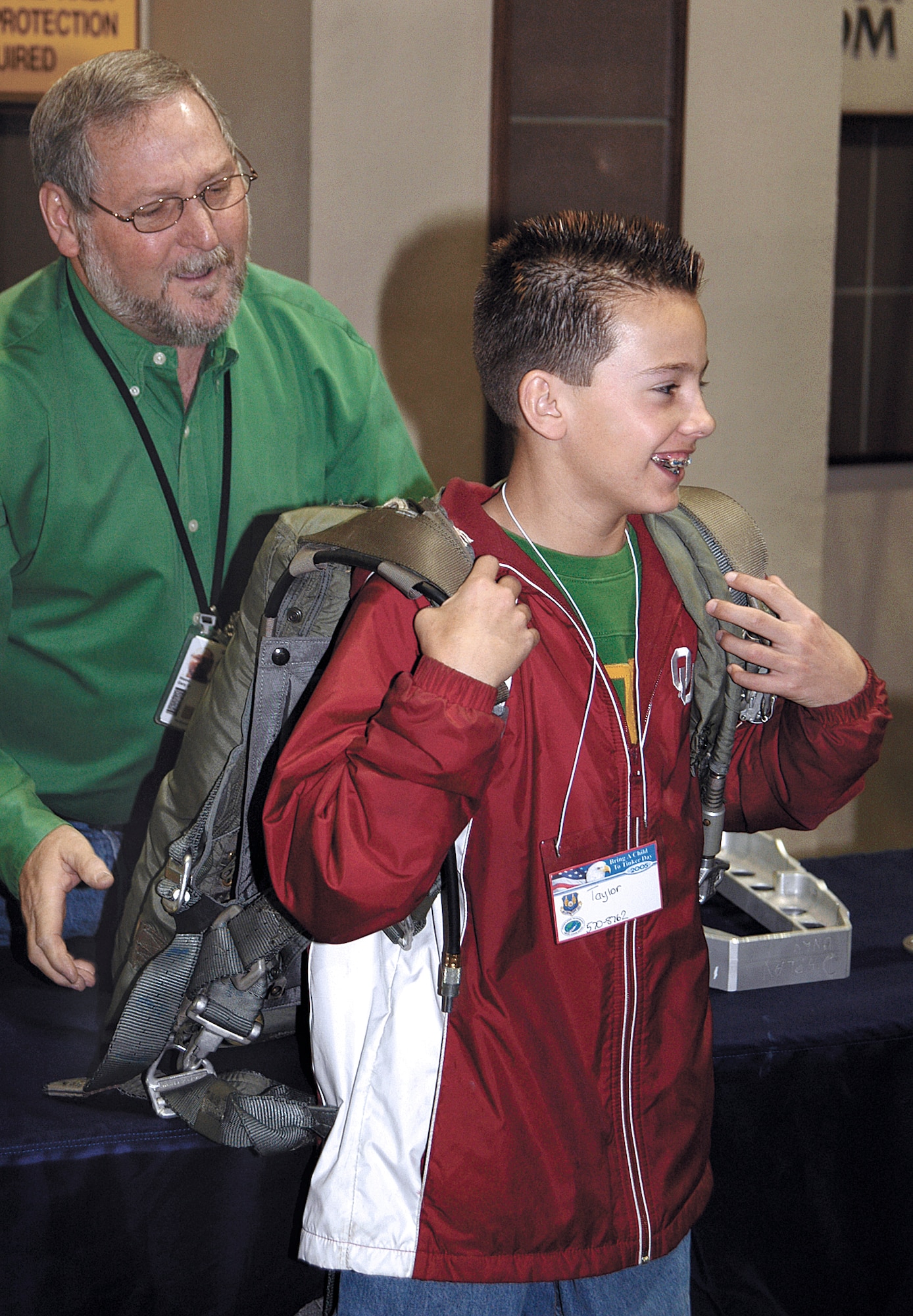 TINKER AIR FORCE BASE, Okla. --  Gary Wood, a parachute shop fabric worker, helps 12-year-old Taylor Welchel feel the weight of a parachute during a Bring a Child to Tinker event.  Taylor, whose dad, Jason Welchel, is a pneudraulics fuel systems mechanic, thought the parachute "felt like a school bag, with a whole lot of books."  The event gave employees a chance to show the children their work world through displays, videos and demonstrations.  (U.S. Air Force photo by Margo Wright)