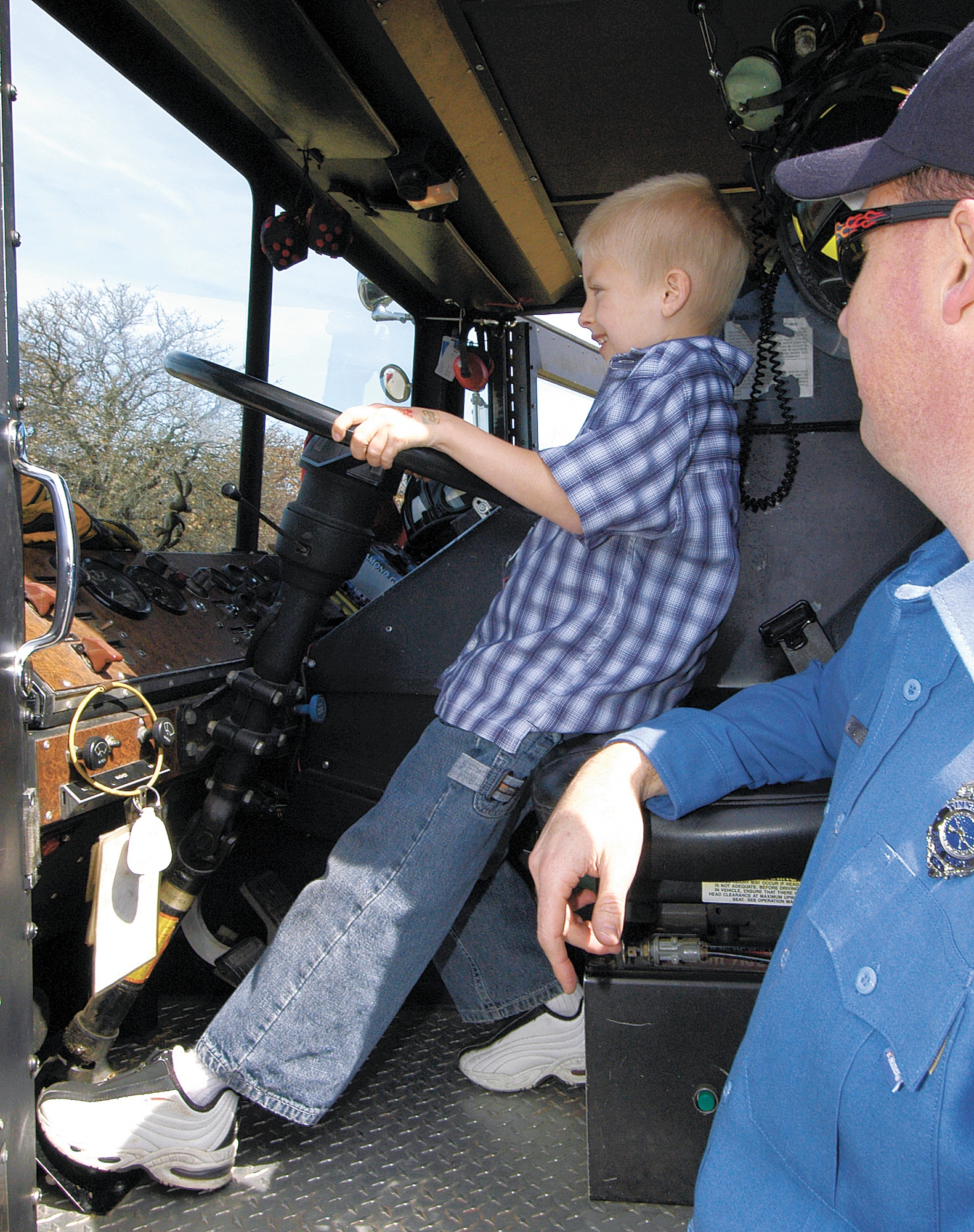 TINKER AIR FORCE BASE, Okla. -- Ben Cuzzort, 9, stretches to reach the floor horn of a fire truck during a Bring a Child to Tinker event.  Firefighter David Langford watches the pint-sized firefighter behind the wheel.  The event gave employees a chance to show the children their work world through displays, videos and demonstrations.  (U.S. Air Force photo by Margo Wright)