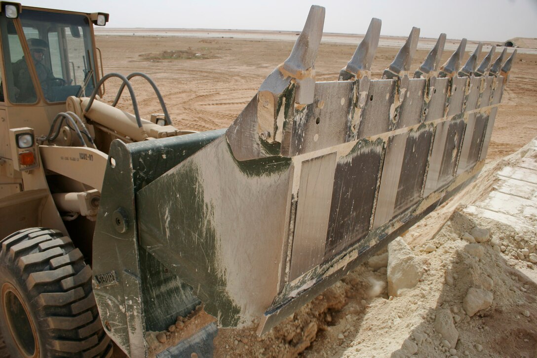 AL ASAD, Iraq -- Lance Cpl. Casey J. Lazaruk, a heavy equipment operator with Marine Wing Support Squadron 271, maneuvers the 'bucket' of a tractor, rubber-tired, articulated steering, multipurpose (TRAM) to pack stockpiling material as he builds a fuel berm near one of the runways here March 30.  The ?Workhorses? of MWSS-271 have gone at it full speed and are finishing building an alternate aircraft-refueling site ahead of schedule.