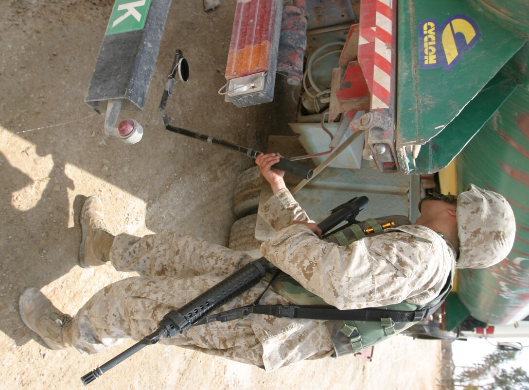 AL ASAD, Iraq--May 4, 2005, Cpl. Caesar D. Clavijo, a clarinet player in the 2nd Marine Aircraft Wing Band from Miami, Fla., searches the underside of a civilian vehicle before allowing it to pass into secure compound here. The 2nd MAW band performs vehicle inspections as part of their duty as a security force while forward deployed.