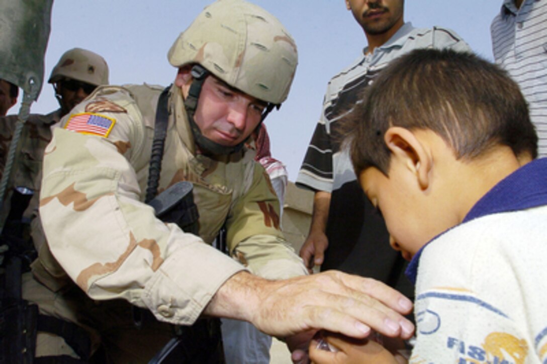 Army Spc. Michael Mize hands out food and candy to an Iraqi boy during a joint patrol and humanitarian aid mission in Al Hillah, Iraq, on May 14, 2005. Mize is attached to the 940th Military Police Company, which is deployed to Iraq from Walton, Ky. 