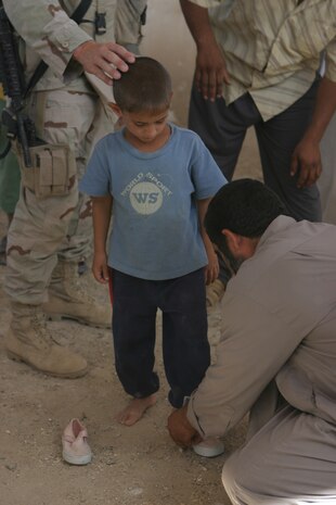 CAMP TAQADDUM, Iraq (May 28, 2005) - An Iraqi child, with the help of his father, tries on a pair of shoes the Soldiers from 3rd platoon, Alpha Company, 2nd Battalion, 112th Armor, 36th Infantry Division, brought to the village of Al Kabani.