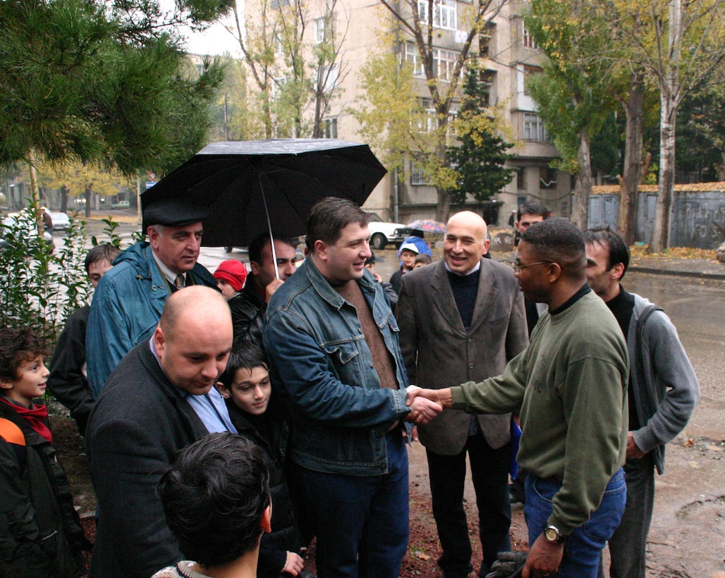 Republic of Georgia capital city Tbilisi City Mayor Gigi Ugulava greets Maj. Melvin Chattman, 38, the Georgia Sustainment and Stability Operations Program U.S. task force commander and native of Memphis, Tenn., at the Waldorf Free School, Nov. 5. Task force members donated an oak tree, bushes, flowers, axes and their personal time to improving the school grounds for the children in addition to splitting firewood to heat the school. Flanking the mayor are (left) Levan Khelaia, the school environmental coordinator, and (right) Jimi Mazanashvili, Parent Teacher Association coordinator. The more than 50-member U.S. task force, many of them veterans of Iraq and Afghanistan, is training Georgian soldiers in preparation for their scheduled deployment to Iraq as Coalition members. Georgia?s GSSOP trained 22nd Light Infantry Battalion troops will form part of the dedicated force called for in UN Security Council Resolution 1546 to protect UN forces in Iraq.