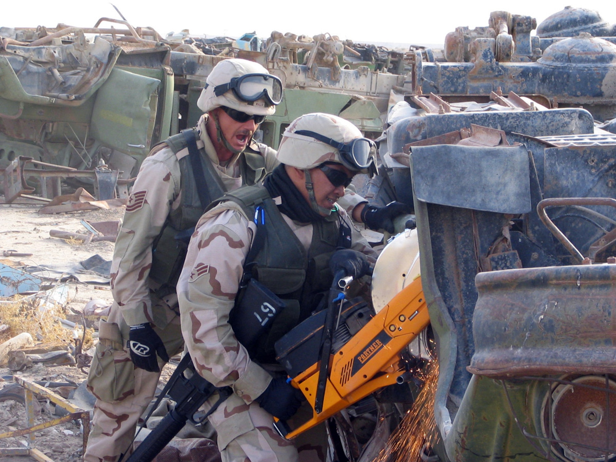 ALI BASE, Iraq (AFPN) -- Airman 1st Class Christopher Cruz practices using a K-12 saw on the hinges of a vehicle as Tech. Sgt. James Ralls (left) looks on. Airman Cruz put his experience to use here when the rescue air mobility squad was called into action. (U.S. Air Force photo by Senior Airman Thomas Knob)
