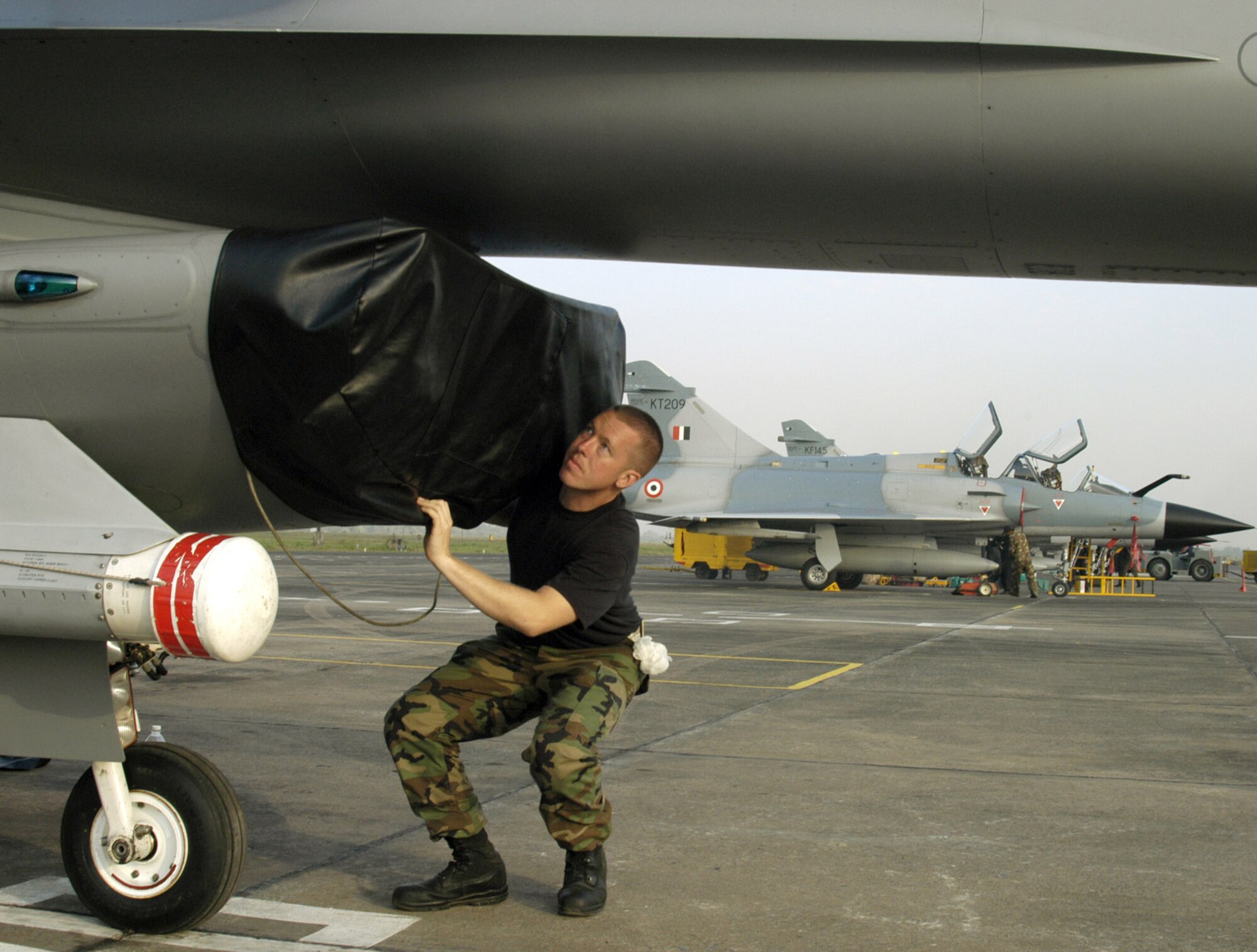 KALAIKUNDA AIR STATION, India -- Crew chief Staff Sgt. Garrett Faust removes the intake cover from his the F-16 Fighting Falcon here. The Falcons are flying dissimilar air combat sorties against Indian Mirage fighters -- like in the background -- and other aircraft during exercise Cope India 06, which ends Nov. 19. The sergeant is from the 35th Aircraft Maintenance Squadron at Misawa Air Base, Japan. (U.S. Air Force photo by Tech. Sgt. Martin Jackson)
