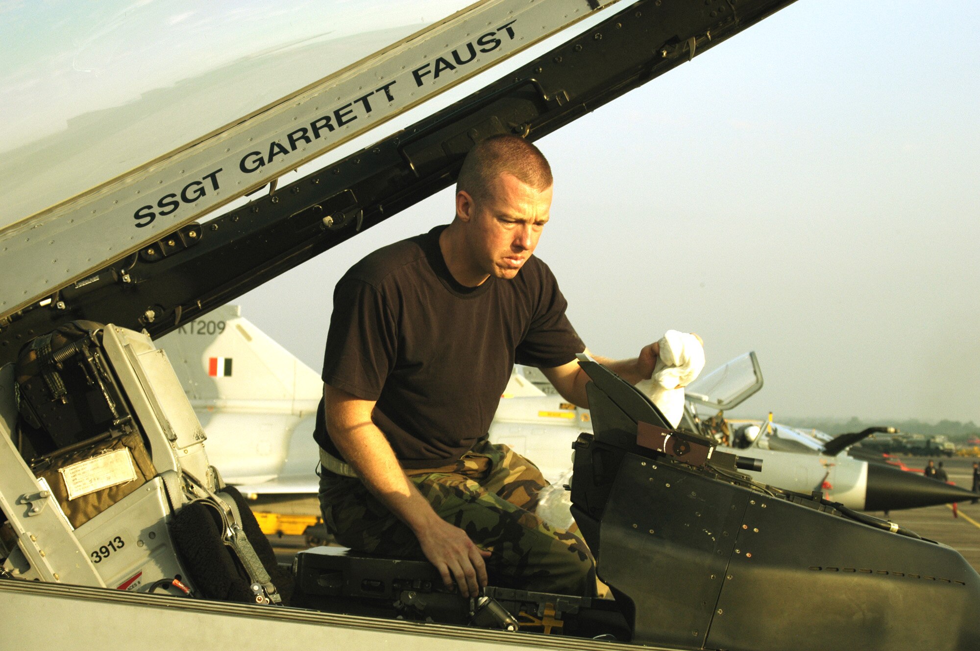 KALAIKUNDA AIR STATION, India (AFPN) -- Crew chief Staff Sgt. Garrett Faust cleans the heads up display on his the F-16 Fighting Falcon here. The Falcons are flying dissimilar air combat sorties against Indian Mirage fighters -- like in the background -- and other aircraft during exercise Cope India 06, which ends Nov. 19. The sergeant is from the 35th Aircraft Maintenance Squadron at Misawa Air Base, Japan. (U.S. Air Force photo by Tech. Sgt. Martin Jackson)
