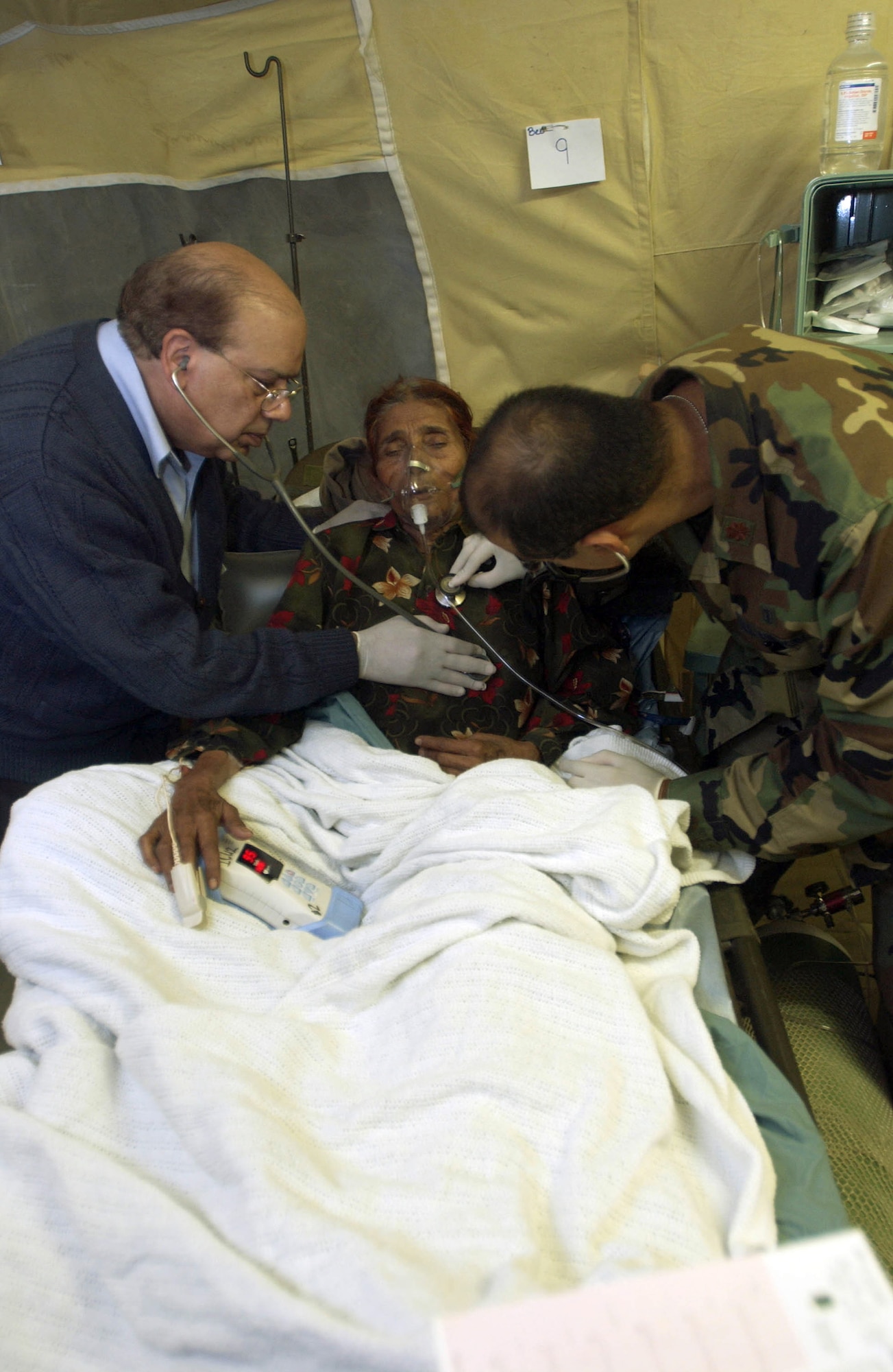 MUZAFFARABAD, Pakistan (AFPN) -- Maj. (Dr.) Fareed Sheikh (right) and his father Dr. Mushtaq Sheikh, a civilian physician, treat a patient at the 212th Mobile Army Surgical Hospital unit here.  Both doctors are Pakistani-Americans.  The hospital is helping with earthquake relief operations.  (U.S. Air Force photo by Staff Sgt. Quinton Russ) 