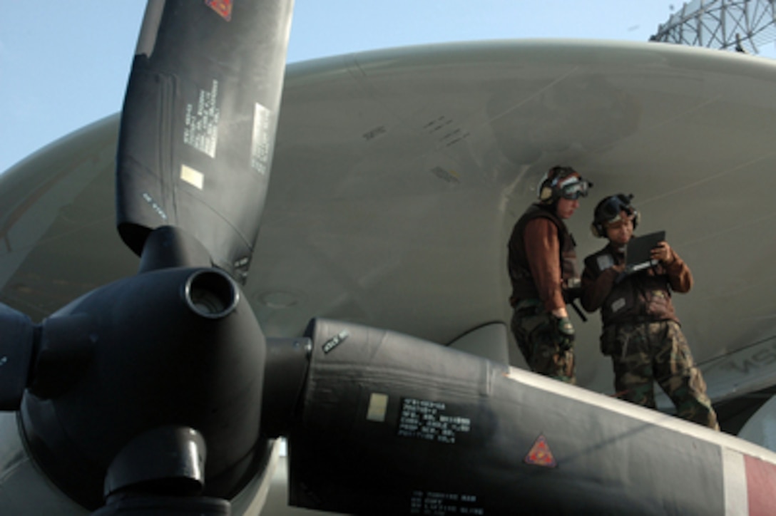 Plane Captain Airman Nathaniel Rich (right) and Airman Ricardo Sawh stand under the shelter of the radar rotodome as Rich instructs his trainee Sawh how to perform a daily inspection on an E-2C Hawkeye on the flight deck of the USS Kitty Hawk (CV 63) on Nov. 7, 2005. The Hawkeye is assigned to Carrier Airborne Early Warning Squadron 115. 