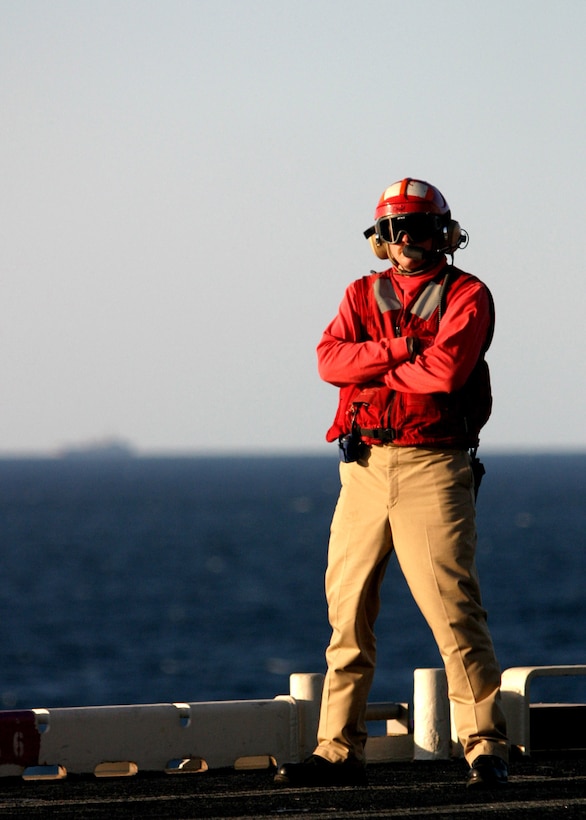 With another amphibious assault ship barely visible in the distance, a Navy chief petty officer supervises Harrier flight operations on the flight deck of the USS Nassau, Dec. 2, 2005.  Embarked on the USS Nassau, Carter Hall, and Austin is the 22nd Marine Expeditionary Unit (Special Operations Capable) which is serving as the landing force for Expeditionary Strike Group 8.::n::