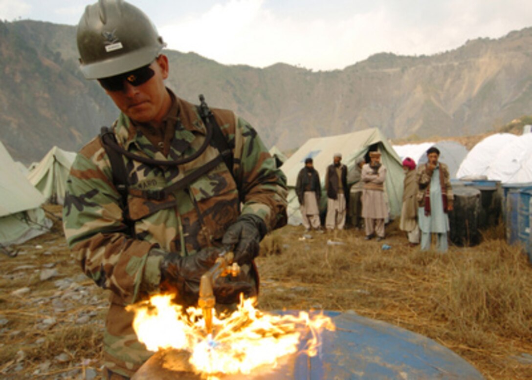 U.S. Navy Petty Officer 3rd Class Chad Seward uses a cutting torch to cut through a barrel as Navy Seabees build latrines for displaced families at the Thuri Park Tent Village near Muzaffarabad, Pakistan, on Nov. 11, 2005. Seward is a Navy steelworker attached to Naval Mobile Construction Battalion 74, deployed from Gulfport, Miss. The Department of Defense is supporting the State Department by providing disaster relief supplies and services following the massive earthquake that struck Pakistan and parts of India and Afghanistan. 