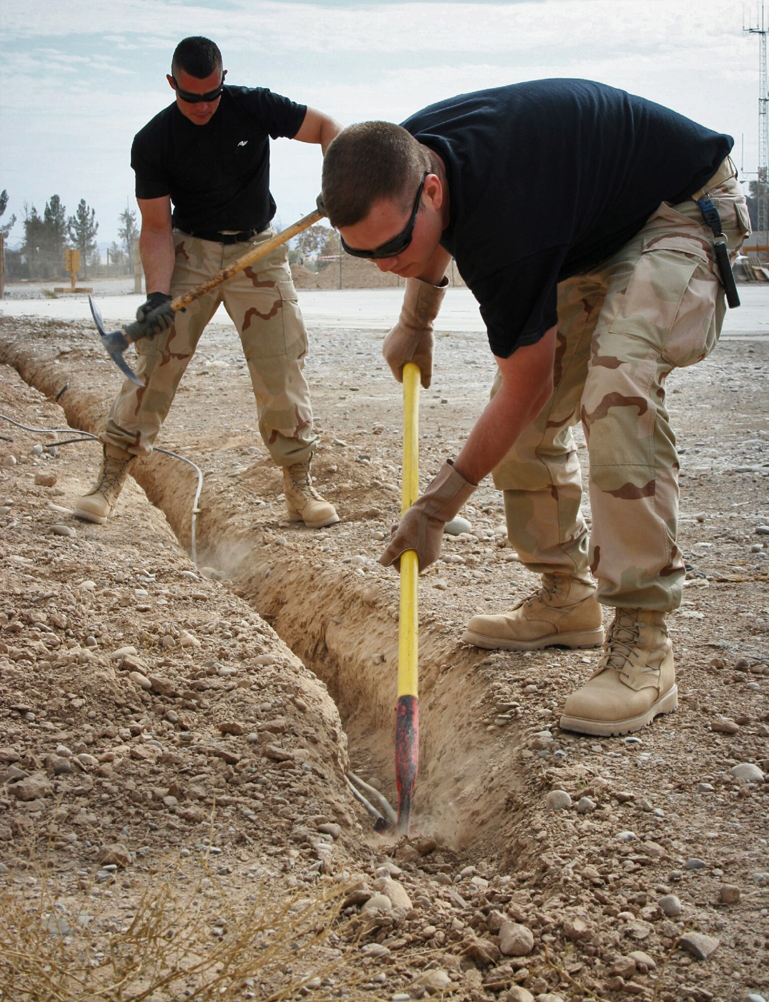 KANDAHAR AIR FIELD, Afghanistan (AFPN) -- Staff Sgt. Jeremy Bellard (left) and Senior Airman Jeffrey Shipley help dig a ditch for relocating 2,400 feet of radar fiber and computer network and phone cable. As U.S. forces prepare to return control of the airport terminal and tower to Afghan control, combat communicators have installed more than a mile of copper and fiber cabling. Sergeant Bellard, from Church Point, La., is deployed from the Hammond Air National Guard Station in Hammond, La. Airman Shipley, from Baton Rouge, La., is also deployed from Hammond ANG Station. (U.S. Air Force photo by Staff Sgt. Marcus McDonald) 