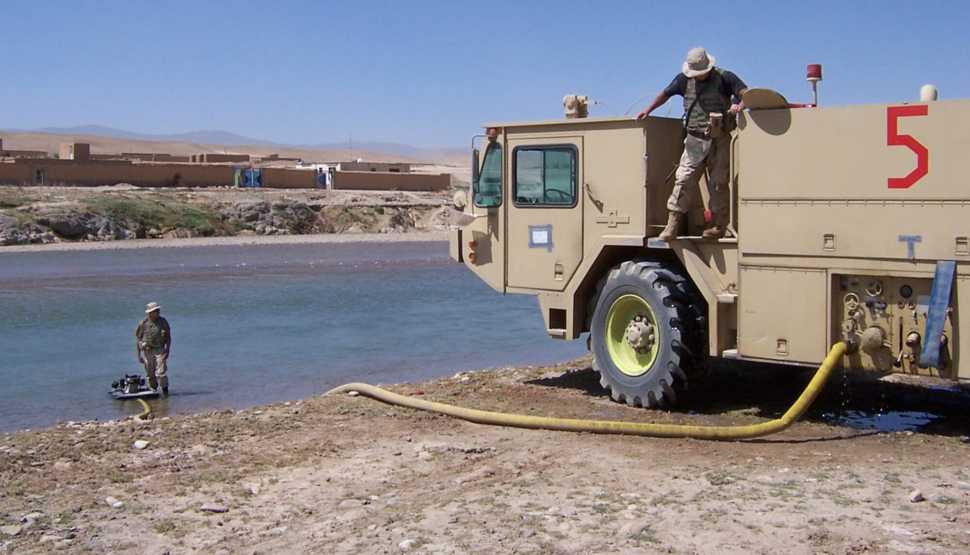 CHAGCHARAN, Afghanistan (AFPN) -- Senior Airmen Victor Cardenas and Michael Sandoval refill the water tanks on their fire truck from a local stream near Chaghcharan, Afghanistan. The Airmen are part of a six-man fire rescue team assigned to the air field. The team -- the only one of its kind in Afghanistan -- provides rapid-reaction airfield rescue and fire-fighting capability. They provided fire protection for the Lithuanian Provincial Reconstruction Team. Both Airmen deployed from Ramstein Air Force Base, Germany. (U.S. Air Force photo by Master Sgt. Kevin Riehle)