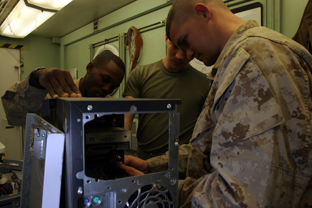 Sergeant Christopher R. Cales, Cpl. William T. Ryder and Cpl. Warren Douglas, all with Marine Aviation Logistics Squadron 26?s Aviation Information Systems Department, repair a computer.  The Marines and their equipment serve an important communications role in the operation of the 2nd Marine Aircraft Wing (Forward).