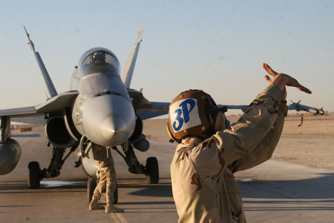 Airman Levi Fackler, an aviation machinist mate and Vassar, Mich., native, communicates through hand signals with Cmdr. Joseph Jerauld, commanding officer of Navy Strike Fighter Squadron 15, during a preflight inspection, Nov. 24, in Al Asad, Iraq. A detachment of Sailors from VFA-15 recently came ashore to continue flight operations during the USS Theodore Roosevelt?s port call in Dubai.