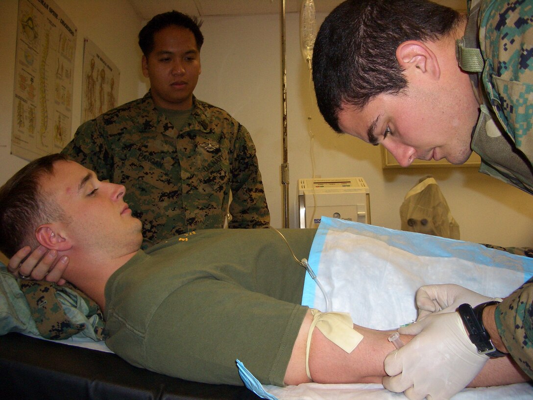 Petty Officer 3rd Class David Michael, plays patient as Petty Officer 2nd Class Thomas Allen demonstrates how to properly insert an IV to Petty Officer 2nd Class Jon Pargan and other Marine Wing Support Squadron 374 hospital corpsman prior to teaching a combat aidsman class for Marines.