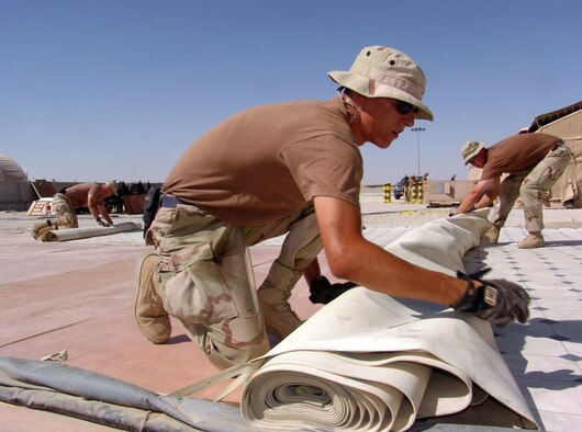 SOUTHWEST ASIA -- Airman 1st Class Steven Owen (left) and Staff Sgt. Troy Strauser roll up linoleum flooring where mess tents once stood to make way for an expanded permanent dining facility at a forward-deployed location.  The Airmen are assigned to the 386th Expeditionary Civil Engineer Squadron and are deployed from Misawa Air Base, Japan.  (U.S. Air Force photo by Master Sgt. Alfred A. Gerloff Jr.)