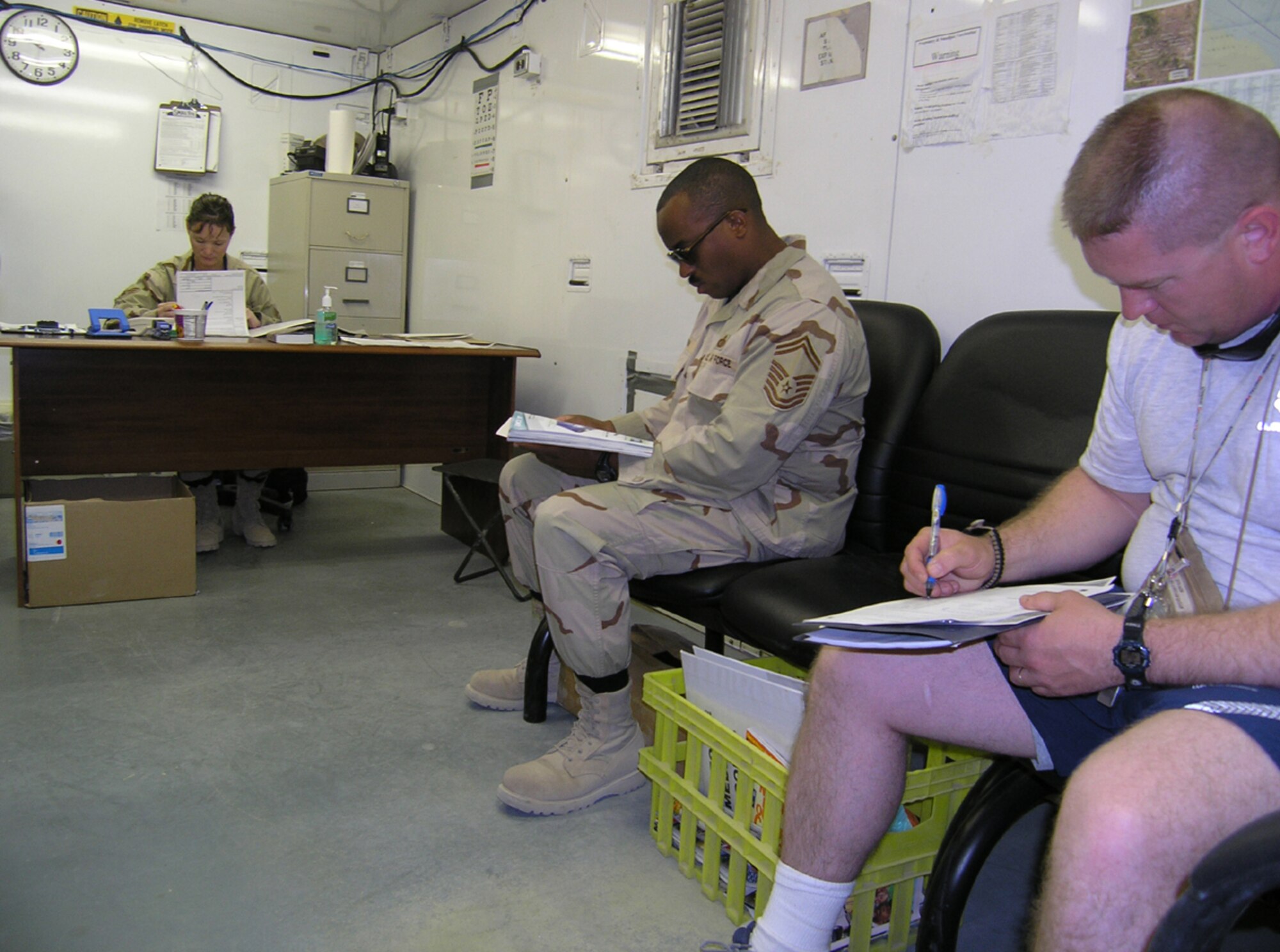 ALI BASE, Iraq -- Senior Master Sgt. Glen Saxon (center) and Master Sgt. Timothy Vollmerhausen relax in the waiting area as Senior Airman Dora Sherrill (left) takes care of administrative tasks in the recently expanded base medical clinic here. (U.S. Air Force photo by Tech. Sgt. Paul Dean)
