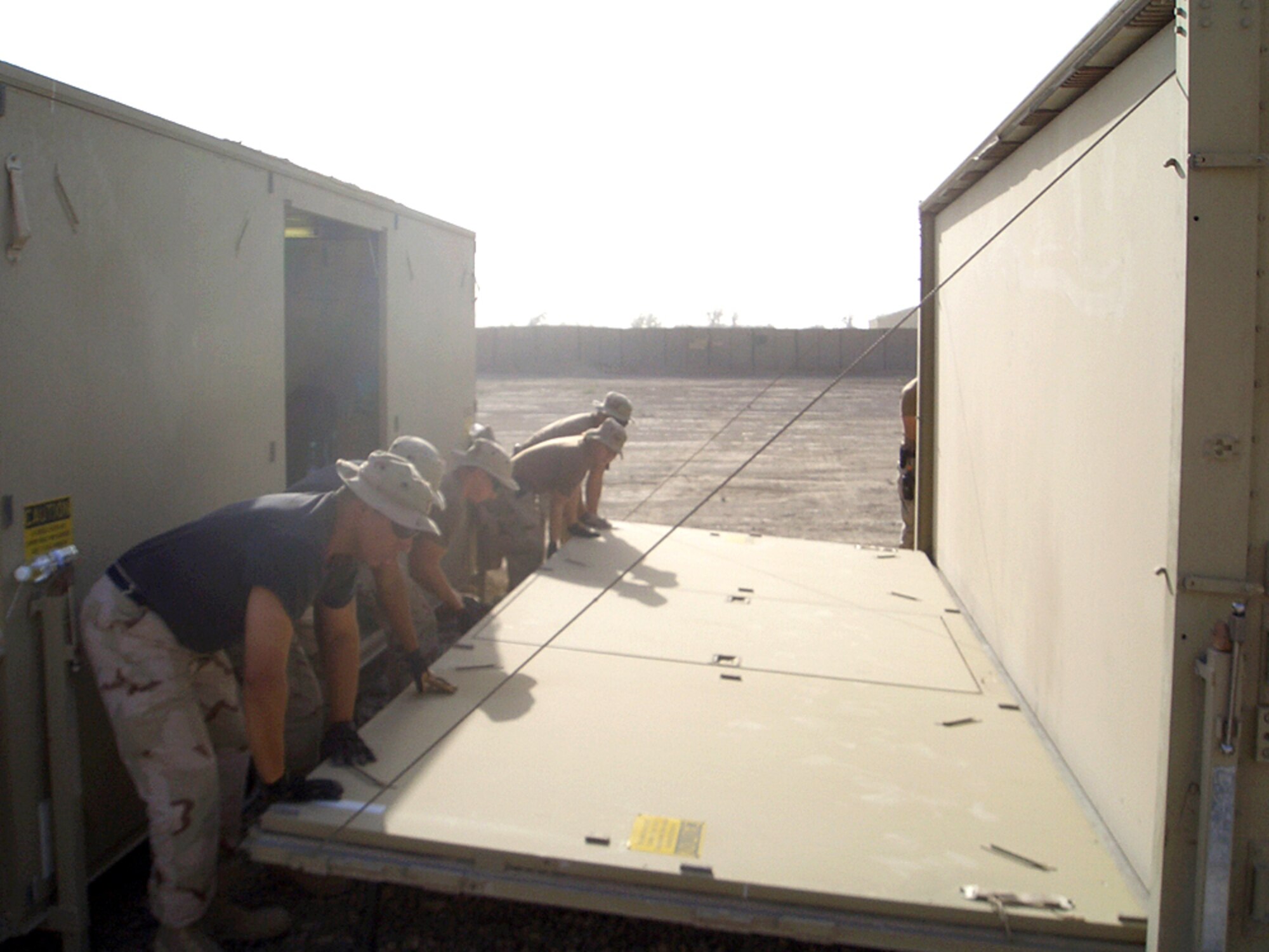 ALI BASE, Iraq -- Airmen lower the floor panel and vertical wall that supports the roof and ties the side walls of an expandable storage container. The new container is part of the recent expansion of the base medical clinic here. (U.S. Air Force photo by Senior Airman Dora Sherrill)
