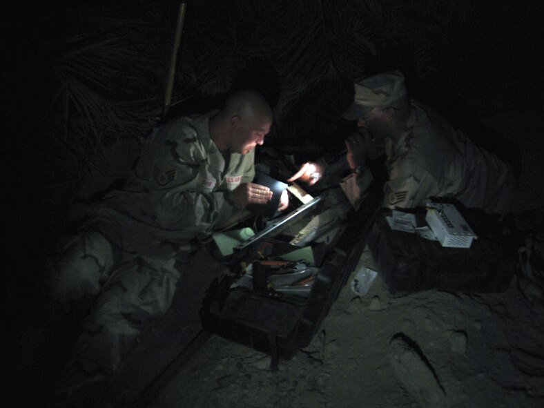 ALI BASE, Iraq -- Staff Sgts. Gary Sayre (left) and Paul Mattke use a flashlight while working to get the 407th Personnel Support for Contingency Operations section's communications back online.  They are assigned to the 407th Expeditionary Communications Squadron.  Sergeant Sayer is deployed from McChord Air Force Base, Wash., and Sergeant Mattke is deployed from Ellsworth AFB, S.D. (U.S. Air Force photo by 1st Lt. Adam Pudenz)