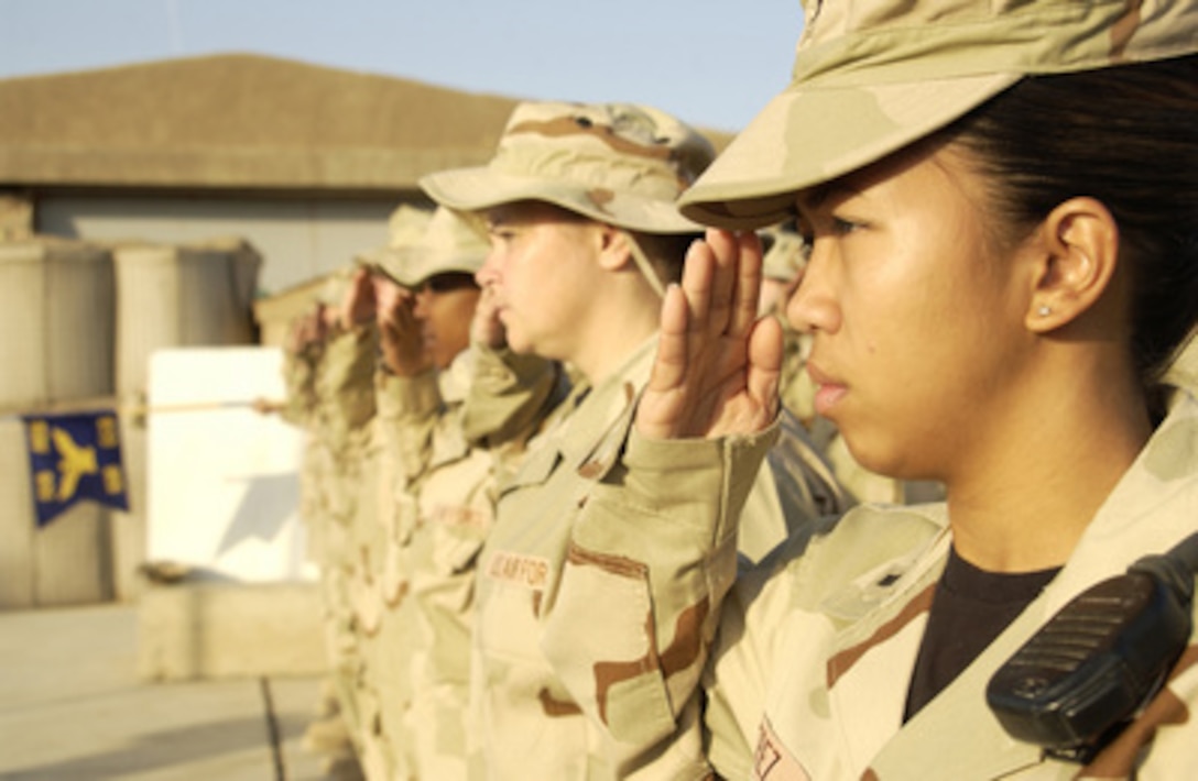 U.S. Air Force 1st Lt. Christina Perez (right) salutes the flag during reveille at Kirkuk Air Base, Iraq, on Oct. 10, 2005. Perez is deployed from Davis Monthan Air Force Base, Ariz., and assigned to the 506th Expeditionary Communications Squadron. 