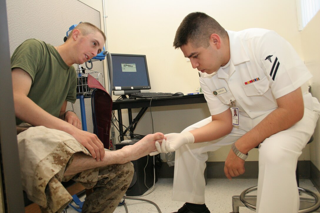 Seaman Larry Garcia, corpsman, military sick call takes a look at the foot of Pvt. Mark C. Machesky, student at the Marine Corps Communications-Electronics School at the Combat Center here. Garcia examined one of many cases of foot problems corpsmen see throughout the day. Corpsmen have been around for centuries to give aid to troops whenever needed.