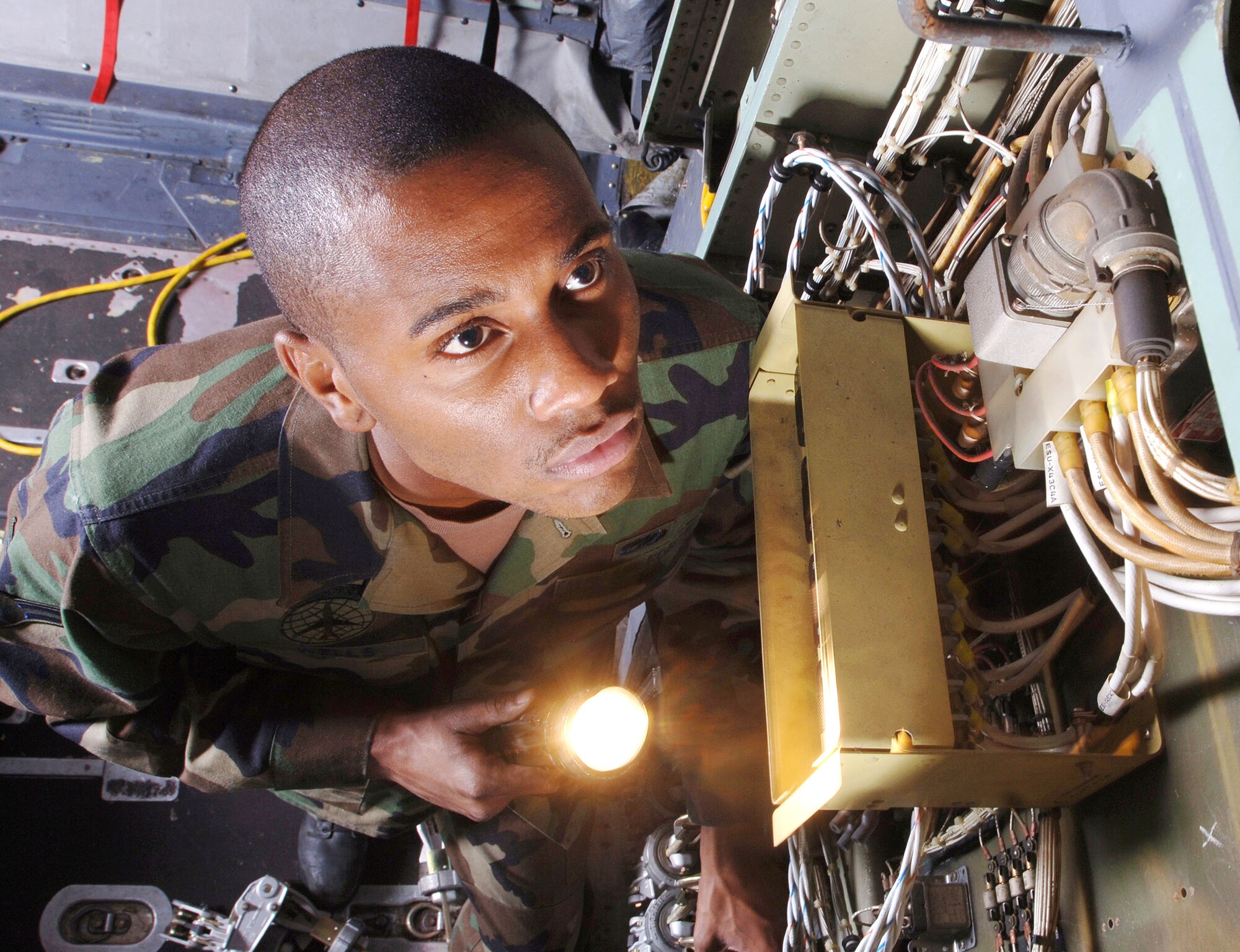 YOKOTA AIR BASE, Japan (AFPN)- Airman 1st Class Marlon Wells uses a flashlight to visually inspect the avionics system in the cargo bay of a C-130 Hercules aircraft here. Airman Wells is looking for chaffed, frayed and disconnected wires to prevent system failure. He is a C-130 crew chief from the 374th Maintenance Squadron/ isochronal section, here at Yokota Air Base, Japan. (U.S. Air Force photo by Master Sgt Val Gempis)