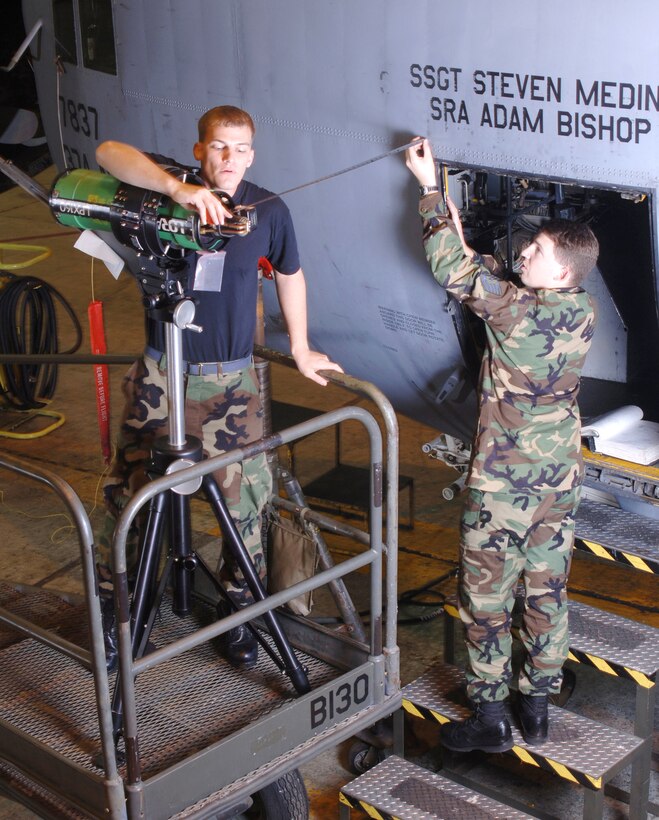YOKOTA AIR BASE, Japan -- Tech. Sgt. Neil Wilke (right) and Senior Airman Jonathan Keller measure the distance between their Lorad portable X-ray equipment and the crew door of a C-130 Hercules aircraft inside a hangar here. The Airmen are checking the door frame for structural cracks. The nondestructive inspection technicians assigned to the 374th Maintenance Squadron here use the X-ray and advanced technology to examine the uniformity, quality and serviceability of components of assigned and in-transit aircraft.  (U.S. Air Force photo by Master Sgt. Val Gempis)