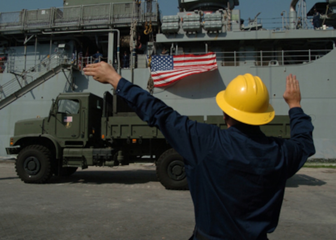 Navy Petty Officer 2nd Class Galen Roberts directs the operator of a crane onboard the USS Pearl Harbor (LSD 52) as it lowers a truck onto the pier in Karachi, Pakistan, on Oct. 18, 2005. The dock landing ship carried the first U.S. Navy shipload of supplies for the Pakistani relief effort. The Department of Defense is participating in the multinational effort to provide humanitarian assistance and support to Pakistan and parts of India and Afghanistan following a devastating earthquake. 