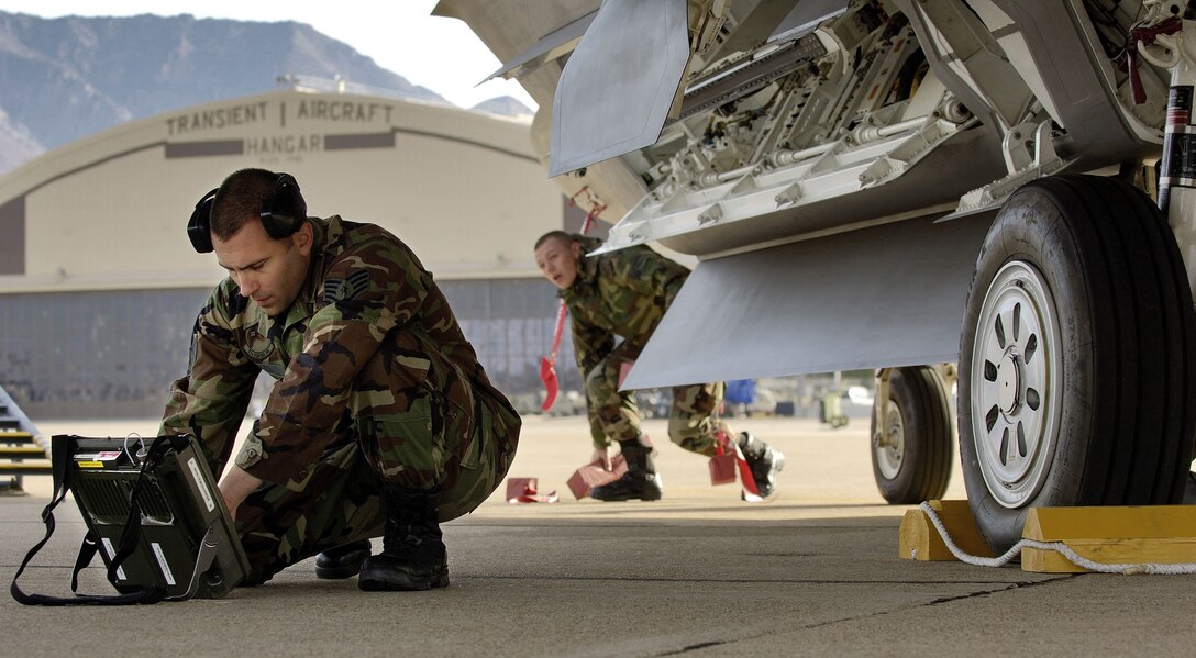HILL AIR FORCE BASE, Utah -- Staff Sgt. Jason McDonald (left), a weapons load crew chief, checks his technical orders after loading two joint direct attack munitions onto an F/A-22 Raptor. The sergeant and the Raptors, from the 27th Fighter Squadron at Langley Air Force Base, Va., deployed here to take part in exercise Combat Hammer. The jets have a twofold goal: complete a deployment and to generate a combat-effective sortie rate away while deployed. (U.S. Air Force photo by Staff Sgt. Samuel Rogers)