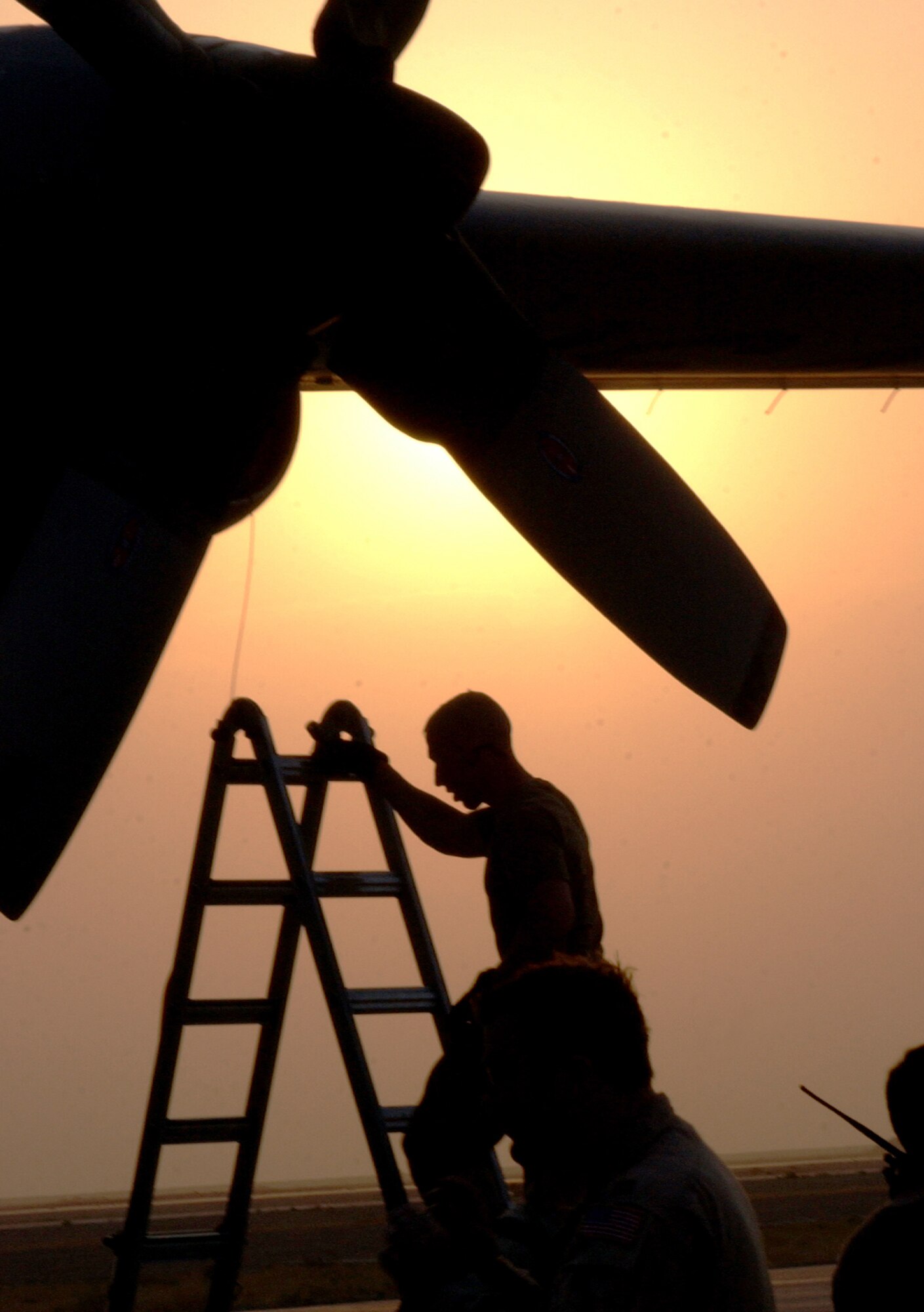 ALI BASE, Iraq -- The sun sets behind Staff Sgt. Bud Sommerville and his C-130 Hercules on the on the aircraft ramp here. Sergeant Sommerville -- of the 777th Expeditionary Airlift Squadron -- went up the step ladder Oct. 18 to install an inlet plug in the transport's engine housing. This base's 407th Air Expeditionary Group operates C-130 Hercules and trains more than 100 Iraqi Airmen on how to maintain and fly the cargo airplanes. (U.S. Air Force photo by Tech. Sgt. Paul Dean)