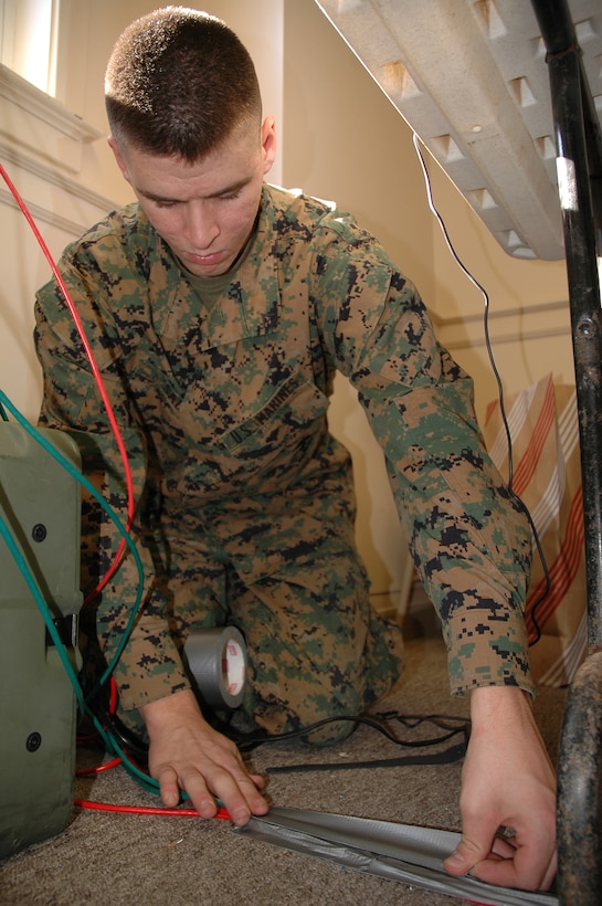 Lance Cpl. John E. Sabia, computer and data network specialist, tapes down local-area network cables after wiring the training site with secured and non-secured internet protocol lines. The command post exercise helped the Marines of the 24th Marine Expeditionary Unit command element gain greater proficiency in coordinating and operating a forward command operations center.